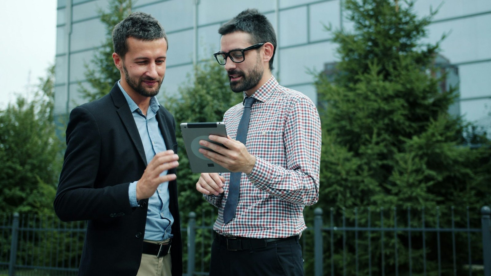Two businessmen looking at a tablet outside office building background