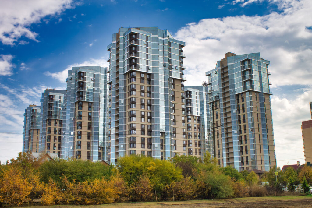 Glass-fronted high-rise apartment towers above autumn trees for Commercial Debt Advisory Firm Costs & Fees | Thorne CRE
